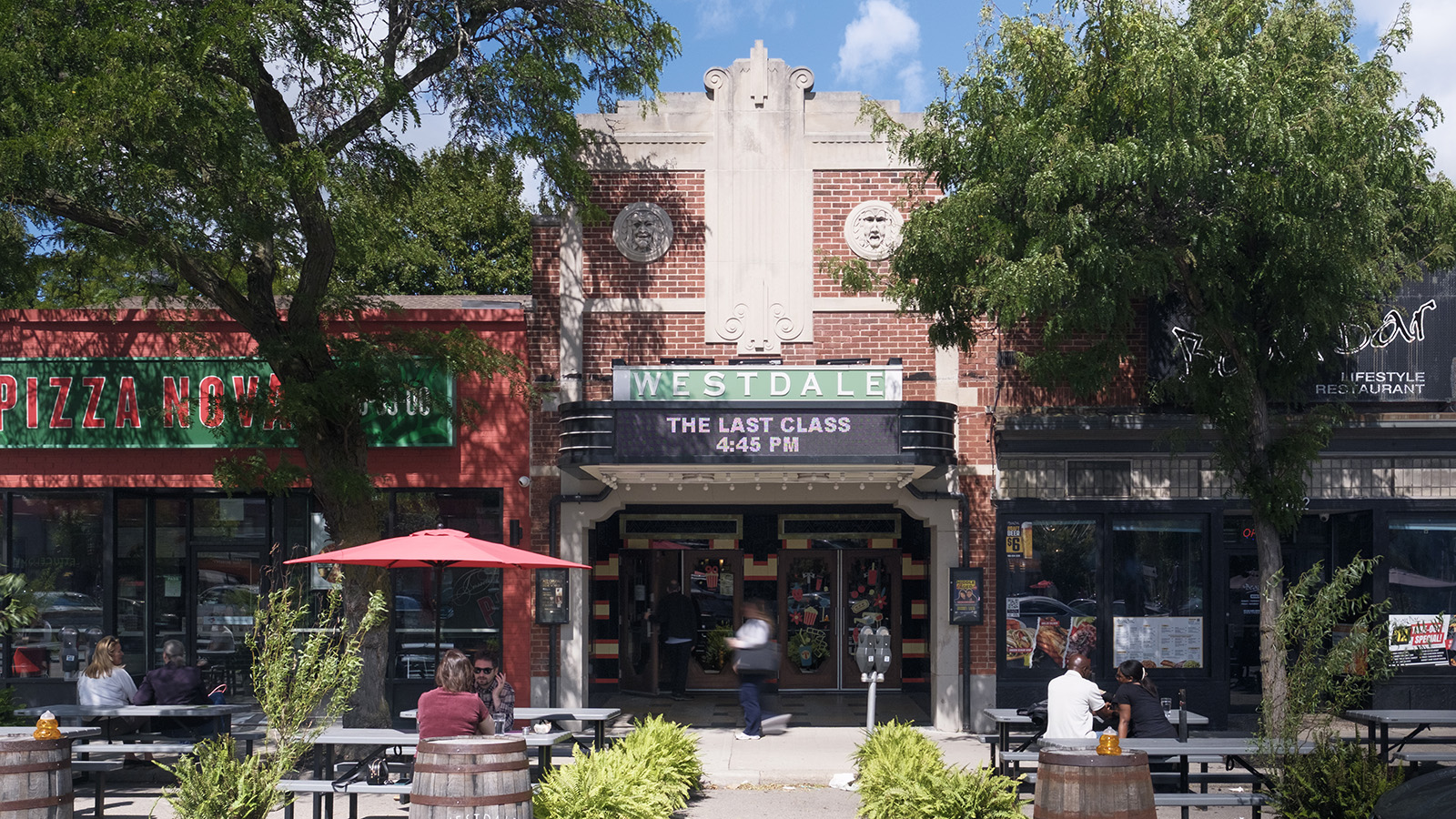 Exterior view of the Westdale Theatre, displaying its new marquee and its integration with neighbouring storefronts, including a pizza place and a restaurant with outdoor seating.